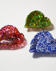 Three hand-blown glass bowls with a heart-like organic shape, shown in red, green, and blue colors with speckled patterns on a white background.