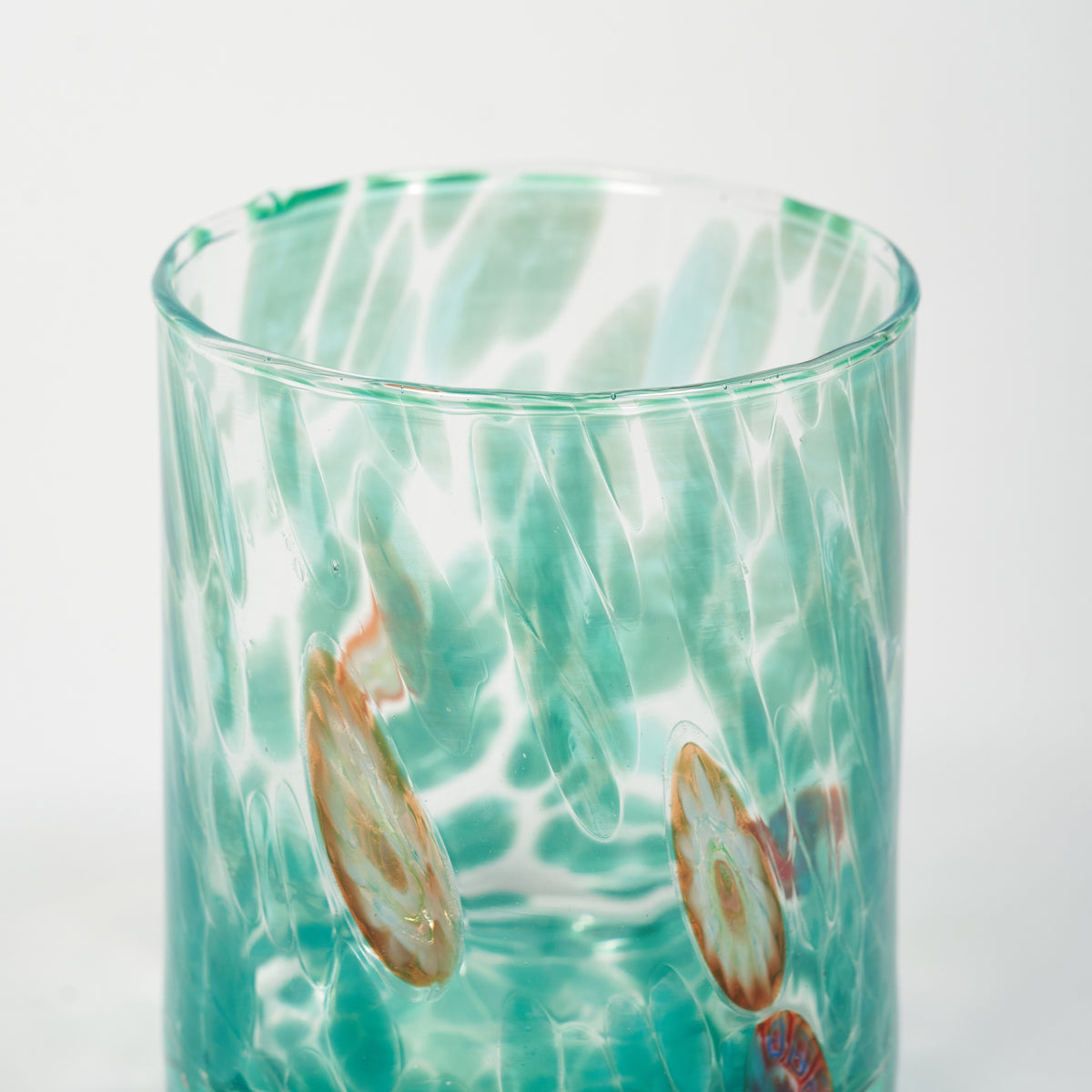 A hand-blown, multicolored Murano glass tumbler with a tapered shape, featuring green, white, and brown swirls.