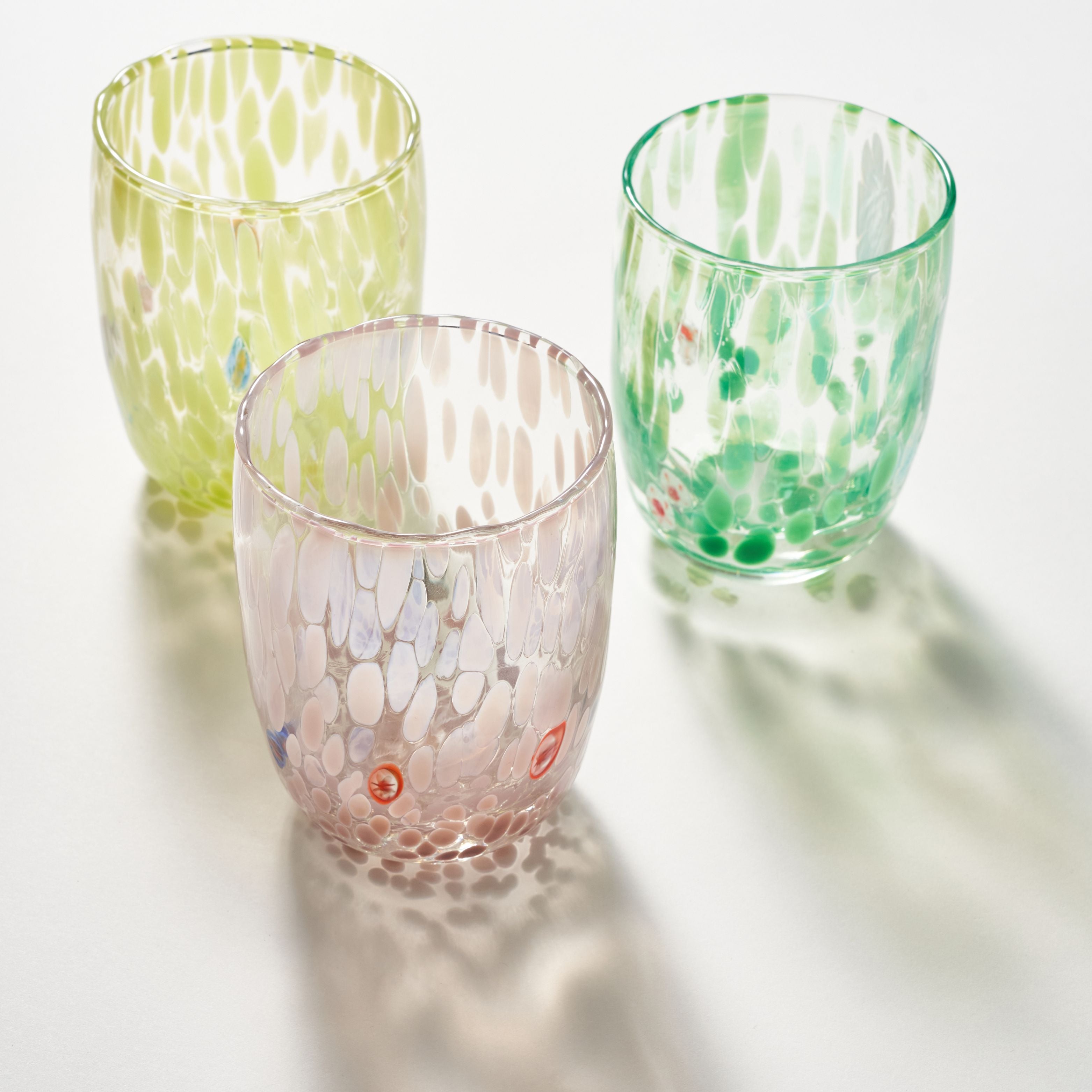 Three textured glass tumblers with organic splatter patterns in pale yellow-green, mint green, and blush pink, arranged on a white surface with soft shadows.
