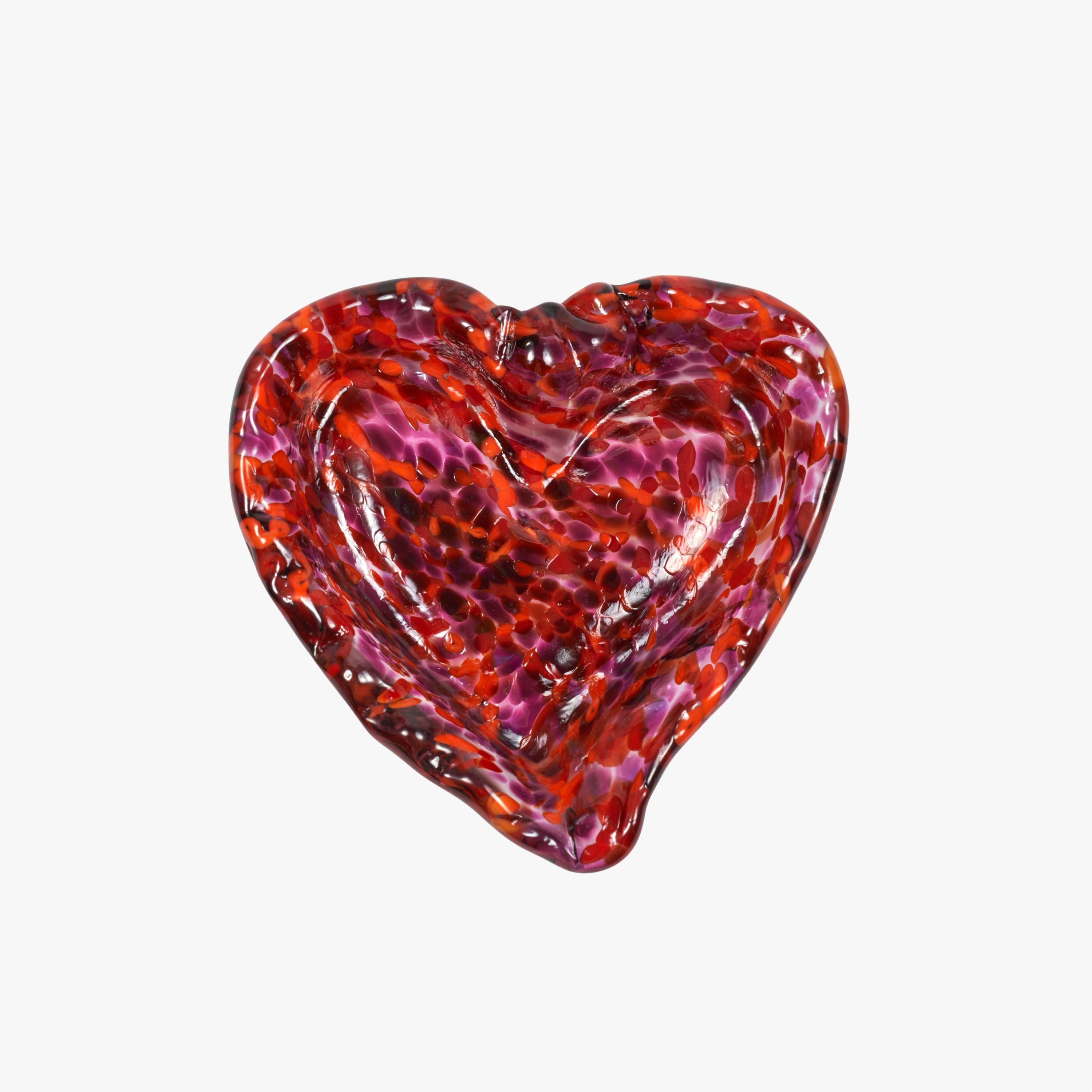 A heart-shaped glass dish with a textured, bubbled pattern in vibrant red, orange, and purple tones, set against a plain light gray background.